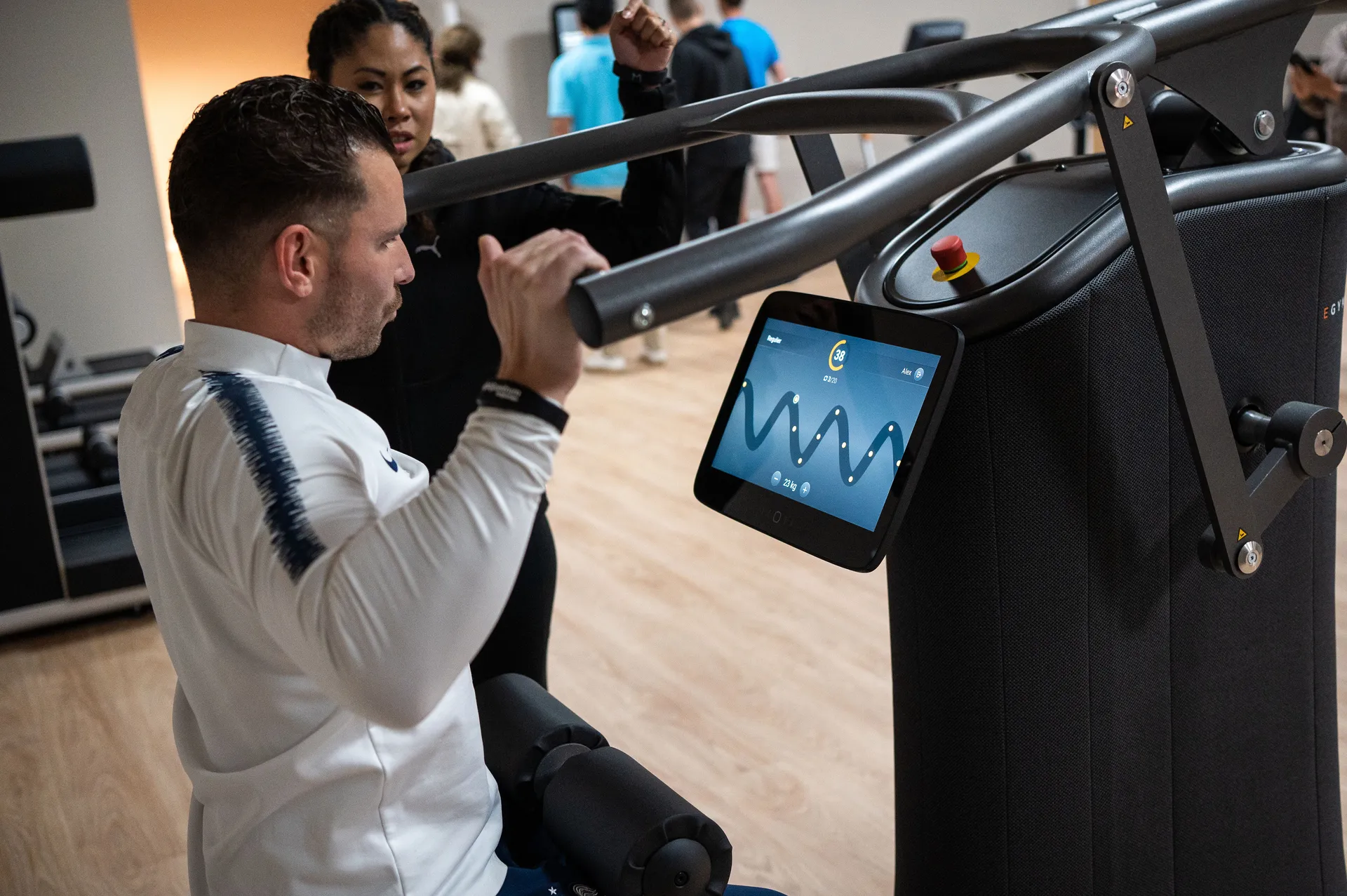 Deelnemer op het E-Gym-toestel, met de coach op de achtergrond